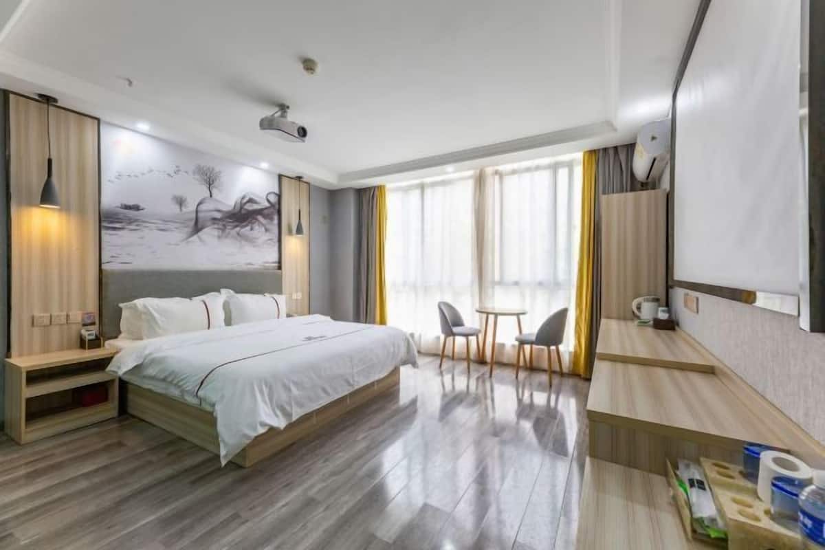 A modern hotel room with a large bed, a desk, and a dining area.