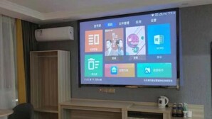 A room with a mounted TV displaying various app icons, a wooden cabinet, and a small table with a coffee maker. - Century Business Hotel (Zuoling New Town) (Wuhan)