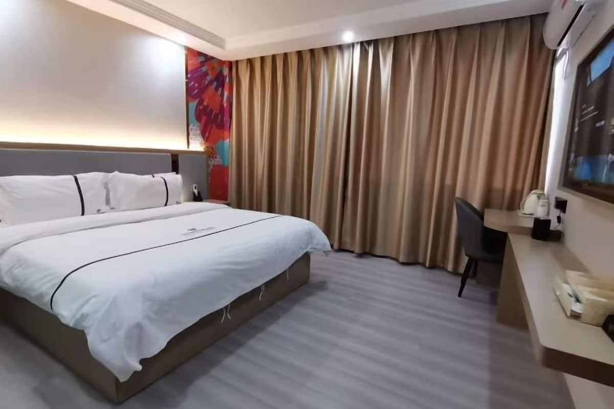 A hotel room with a bed, a desk, a chair, and a large window with curtains.