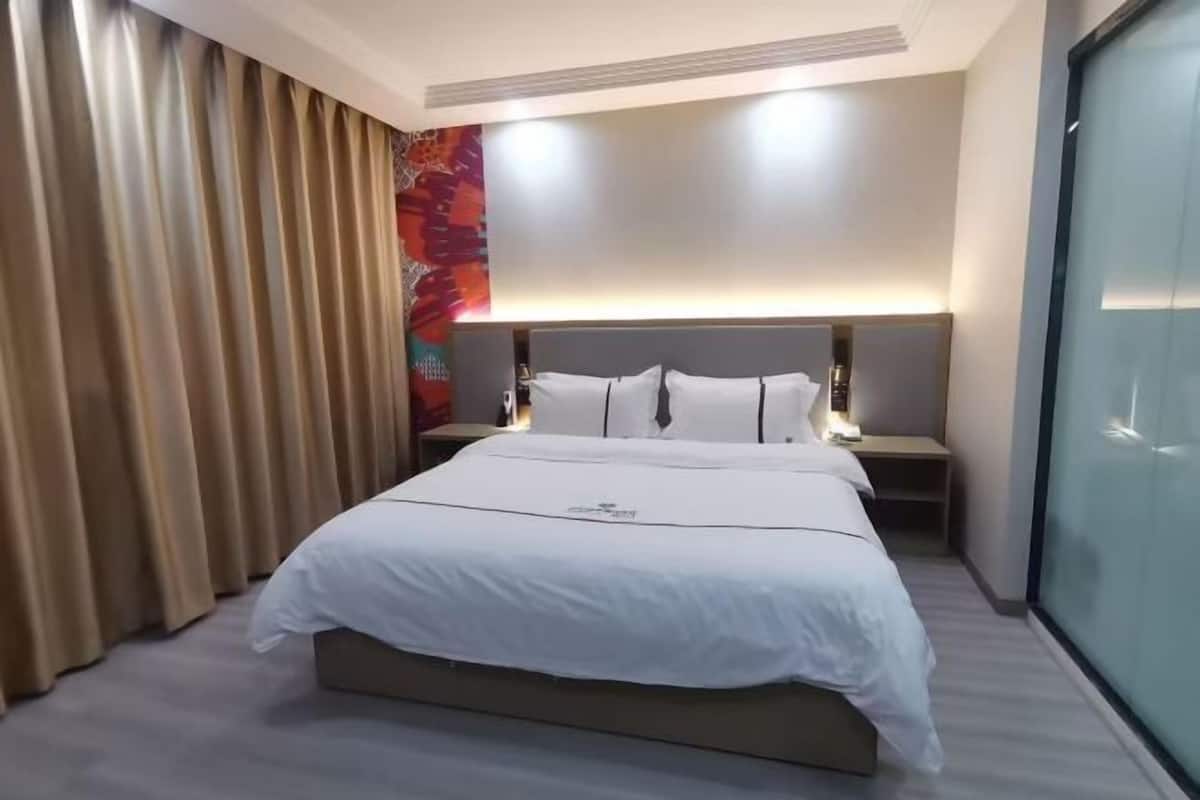A hotel room with a large bed, a headboard, bedside tables, and a curtain.
