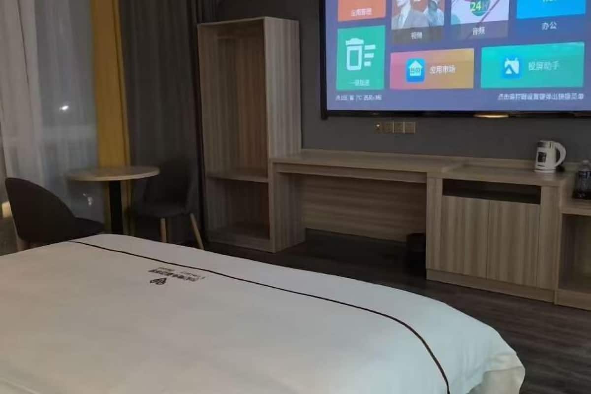 A hotel room with a bed, a TV mounted on the wall, a small table, and a chair.