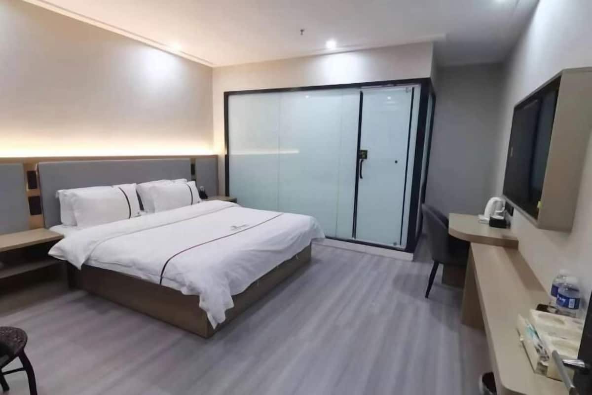 A modern hotel room with a large bed, a desk, a chair, a wardrobe, and a television.