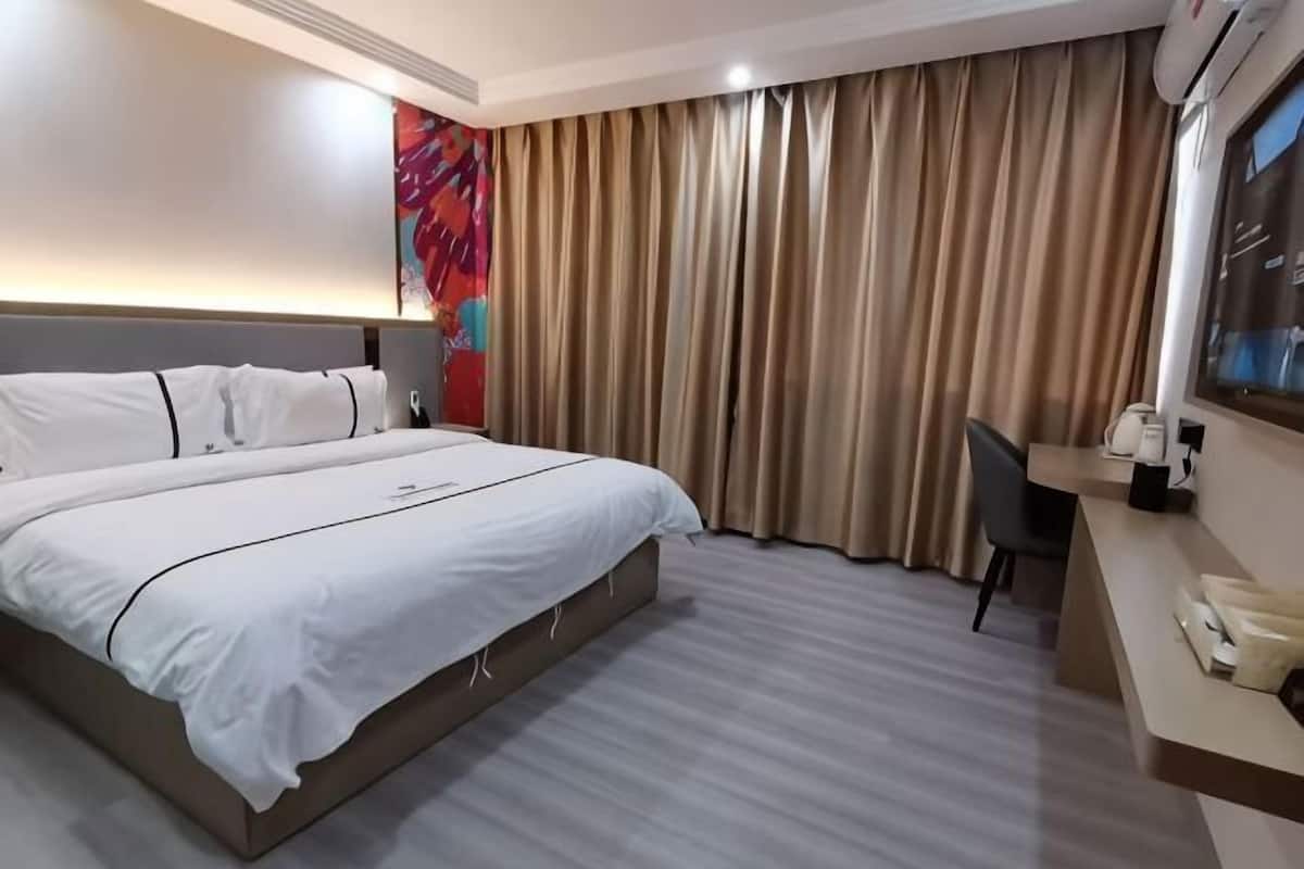 A hotel room with a large bed, a desk, a chair, a television, and a window with curtains.