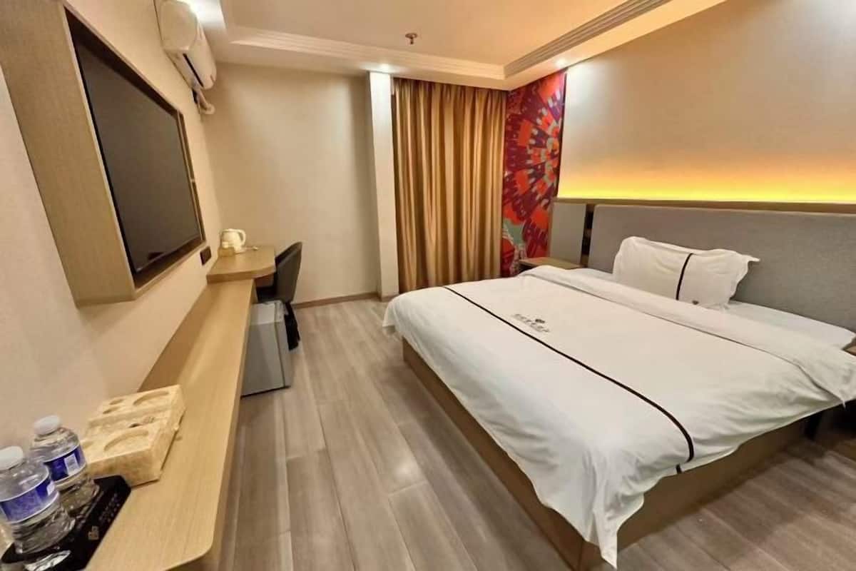 A hotel room with a bed, a desk with a chair, a TV, and a curtain.