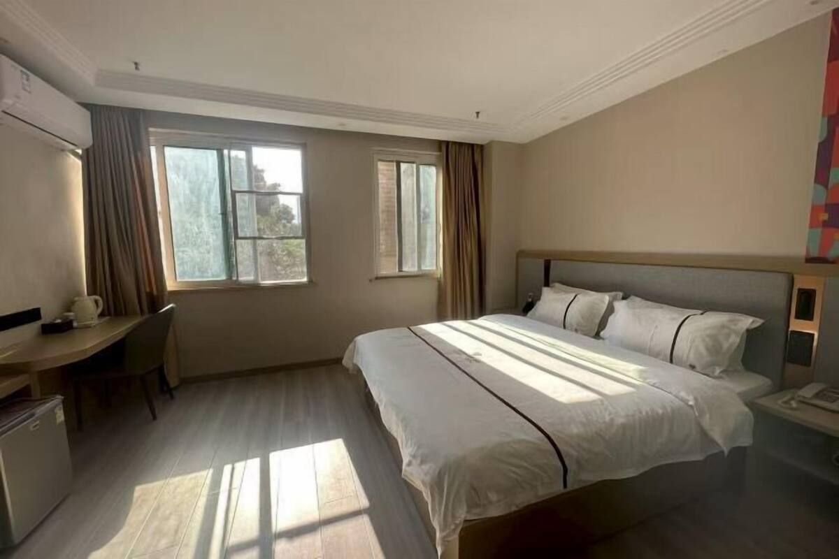 A hotel room with a bed, a desk, a chair, and a window.