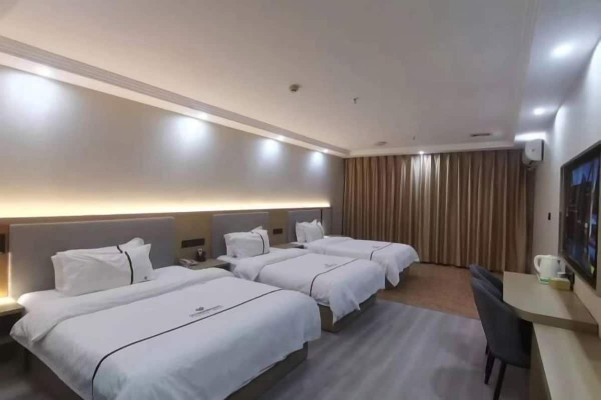 A hotel room with three beds, a desk, a chair, and a large window with curtains.