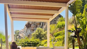 Un'area relax all'aperto coperta, con piscina, pouf in vimini e vista su un paesaggio roccioso.
