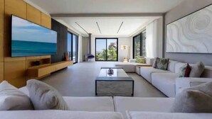 Una sala moderna con un televisor de pantalla plana grande, un sofá modular, una mesa de centro y vistas al exterior a través de amplios ventanales.