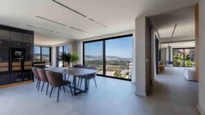 Un'ampia stanza con un grande tavolo da pranzo e sedie, vista sulla città attraverso ampie finestre e una moderna zona cucina.