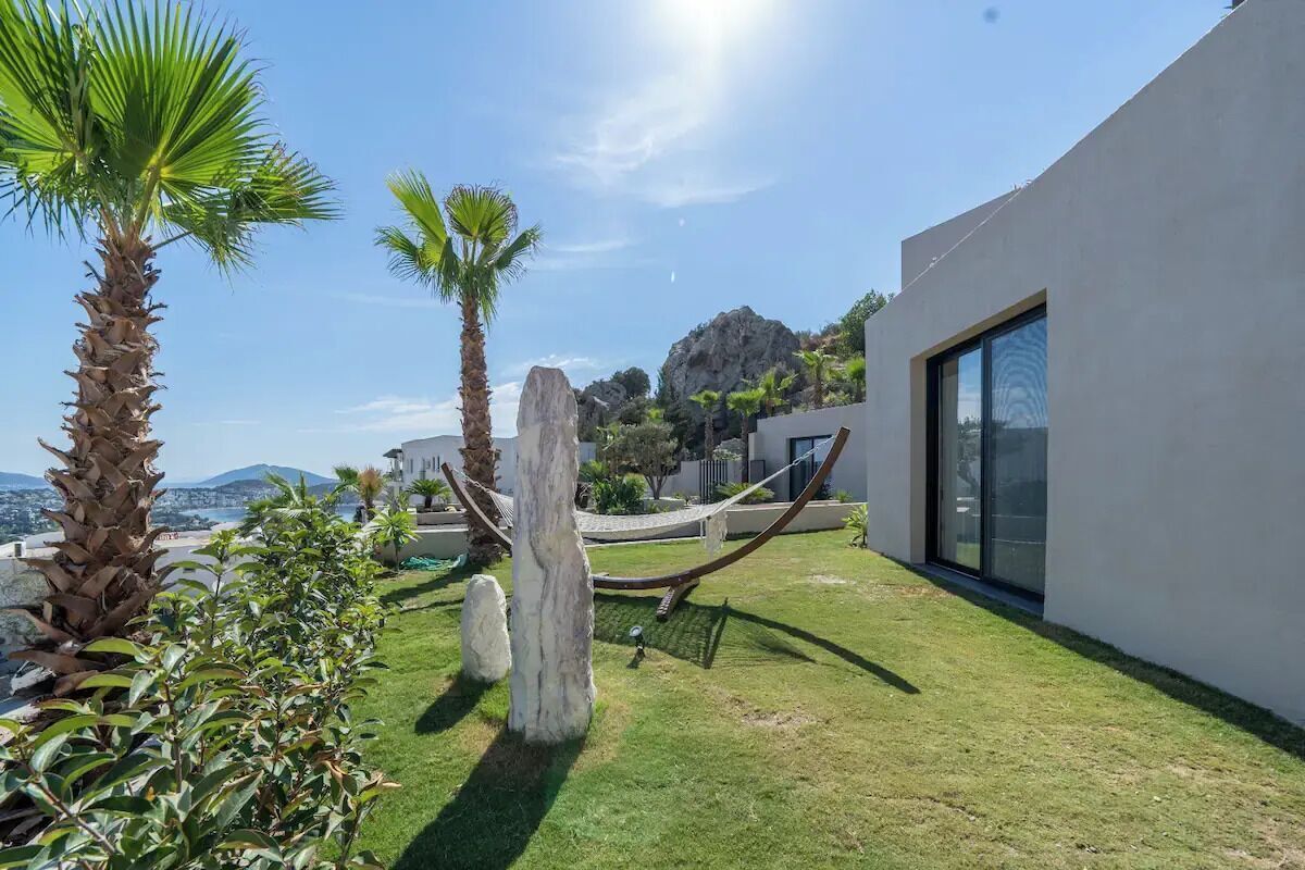 A modern outdoor area with a hammock, palm trees, and a view of the city and mountains.