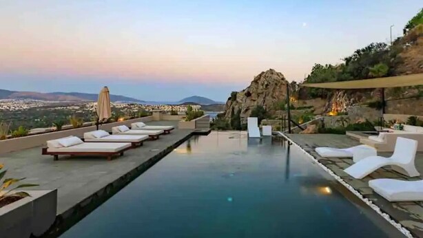 Una piscina a sfioro sul tetto con poltrone relax e vista sulla città e sulle montagne.