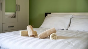 Un lit bien fait, avec des serviettes pliées et une couvre-lit à rayures blanches, dans une pièce aux murs verts et à l’armoire blanche.