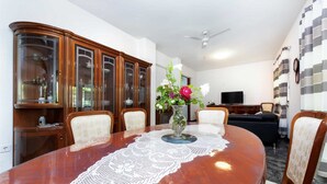 Un coin repas avec une table en bois, des chaises, un vase de fleurs et un téléviseur en arrière-plan.