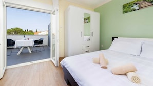 Une chambre à coucher avec un lit, une armoire, un balcon avec une table et des chaises, et un tableau accroché au mur.