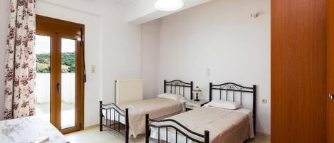 Ein Schlafzimmer mit zwei Einzelbetten, einer Holztür, einem Heizkörper und einem Tisch mit einem Stuhl.