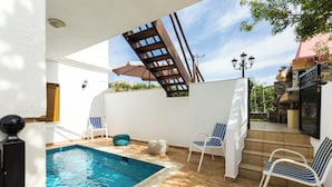 Piscina com deck de madeira, duas espreguiçadeiras e um muro de pedra.