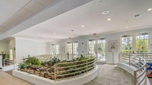 Eine geräumige Lobby mit einem zentralen Garten, weißen Geländern und großen Fenstern, die viel Tageslicht hereinlassen.