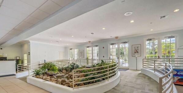 Eine geräumige Lobby mit einem zentralen Garten, weißen Geländern und großen Fenstern, die viel Tageslicht hereinlassen.