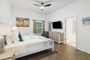 Une chambre à coucher avec un lit, un téléviseur, un ventilateur de plafond, une fenêtre avec des rideaux et une porte.