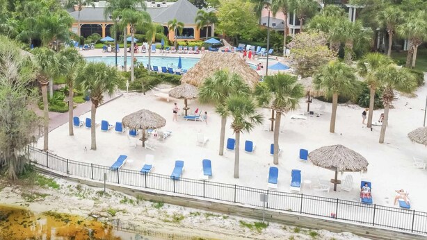 Un complexe hôtelier doté d’une piscine, de chaises longues, de palmiers et d’un petit bâtiment.