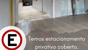 A covered parking area with a reception sign, a gravel driveway, and a building entrance. - Pousada Brunetti (Penha)