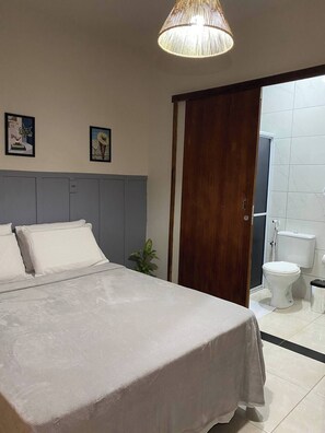 Une chambre à coucher avec un lit, une porte en bois, une salle de bain avec des toilettes et deux tableaux encadrés accrochés au mur.