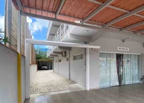 A covered parking area with a reception sign, a gravel driveway, and a building entrance. - Pousada Brunetti (Penha)