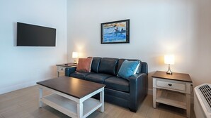 A modern living room with a leather sofa, a wooden coffee table, a flat-screen TV, and two bedside tables with lamps. - Pet Friendly! The Jewel View Cottages Unit 6 (Bigfork)