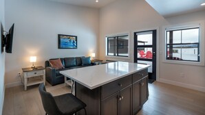 A modern kitchen with a large island, dark cabinetry, and a view of a red chair outside. - Pet Friendly! The Jewel View Cottages Unit 6 (Bigfork)