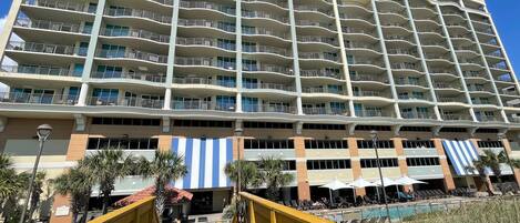 Un hotel de varios pisos con balcones, zona de piscina y mobiliario exterior.