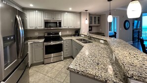 A modern kitchen with granite countertops, stainless steel appliances, and white cabinetry. - MVG 1515 Penthouse 3 Bedroom 3 Bath Ocean View (North Myrtle Beach)
