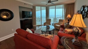 A spacious living room with a flat-screen TV, a fireplace, and a large window offering a view of the ocean. There are two sofas, a coffee table, and a lamp. - MVG 1515 Penthouse 3 Bedroom 3 Bath Ocean View (North Myrtle Beach)