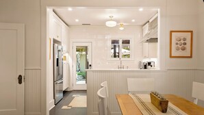 A modern kitchen with white cabinetry, a wooden dining table, and a view of the garden through a window. - Luxury Paso Bungalow • Hot Tub & EV Charger (Paso Robles)