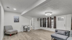 Un salon spacieux avec un canapé gris, un fauteuil à motifs et un bureau blanc.