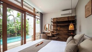 A bedroom with a large bed, a wooden shelf unit, a desk, and a view of a swimming pool.