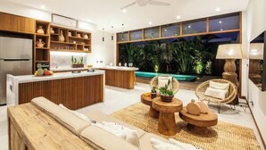 A modern kitchen with wooden cabinets, a central island, and a dining area with a view of a tropical garden.