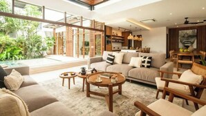 A spacious living area with a large sofa, coffee table, and wooden chairs. There is a kitchen in the background with modern appliances and a dining area with a table and chairs. - Big pool 5 BR Villa Canggu Prime location, 5 min to Berawa beach, . (Tibubeneng)