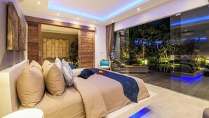 A modern bedroom with a large bed, a glass door leading to a balcony with plants, and a view of the night sky.