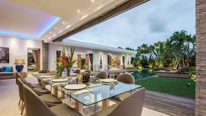 A modern dining area with a glass table and chairs, a pool, and a well-maintained garden.