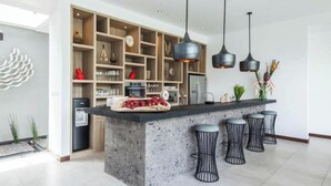 A modern kitchen with a central island, bar stools, pendant lights, and built-in shelving. - Cozy 4 BR Modern Villa in Seminyak, Large Pool, Perfect and Fantastic (Kerobokan Kelod, Kec. Kuta Utara)
