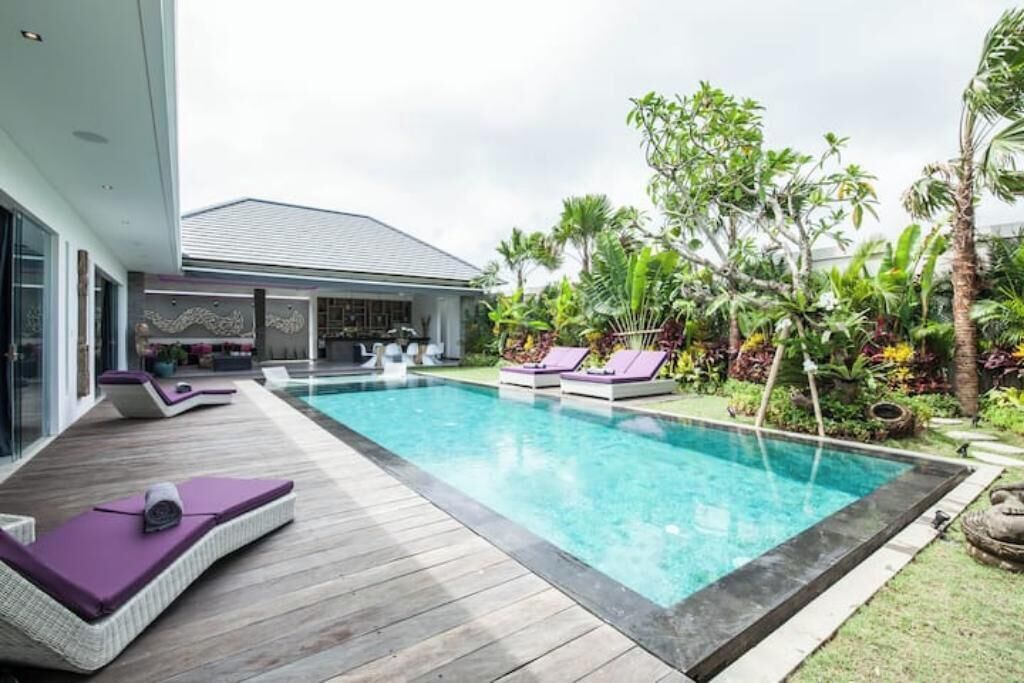 Une maison moderne dotée d’une piscine, de chaises longues pour l’extérieur et d’une végétation tropicale luxuriante.