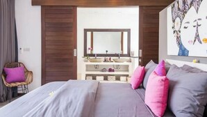 A bedroom with a bed, a vanity with a mirror, and a large painting on the wall. - Cozy 4 BR Modern Villa in Seminyak, Large Pool, Perfect and Fantastic (Kerobokan Kelod, Kec. Kuta Utara)