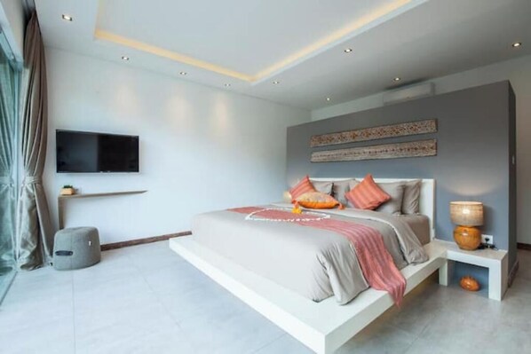 A modern bedroom with a large bed, a flat-screen TV mounted on the wall, and a bedside table with a lamp.
