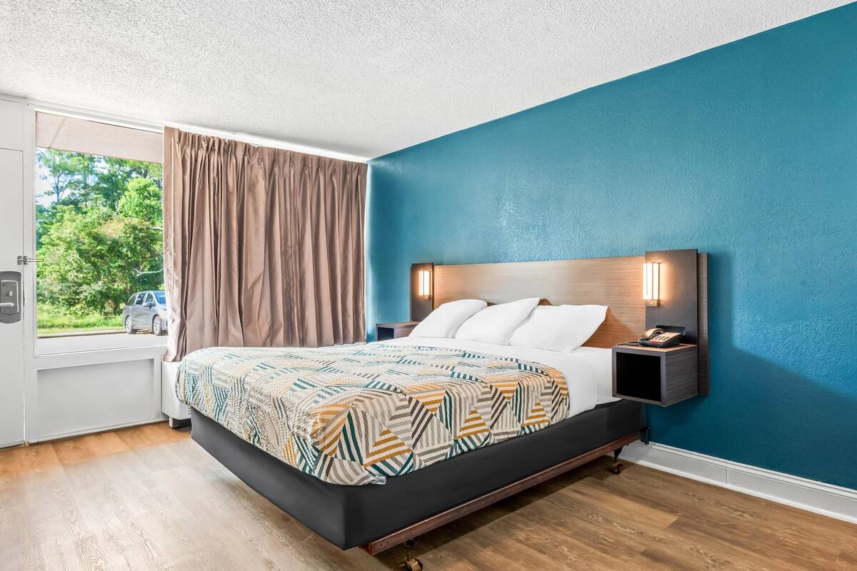 A modern hotel room with a large bed, a nightstand with a phone, and a window with curtains.
