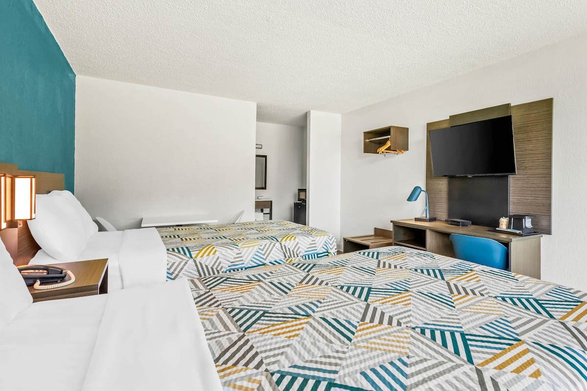 A hotel room with two beds, a desk, a TV, and a bathroom.
