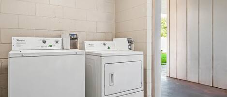A laundry room with two Whirlpool washers and dryers, a white brick wall, and a concrete floor.