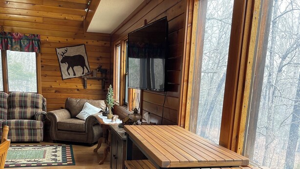 Ein gemütliches Blockhäuschen im Inneren mit einem Holzesstisch, Bänken, einer Couch und einem an der Wand befestigten Fernseher.