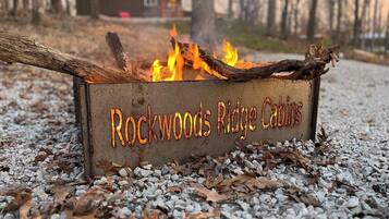 Un foyer extérieur en métal, portant l’inscription « Rockwoods Ridge Cabins », entouré de gravier et de feuilles mortes.