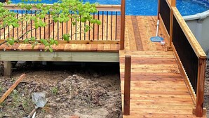 Ein oberirdischer Swimmingpool mit Holzterrasse und Metallzaun, umgeben von einem Wald.