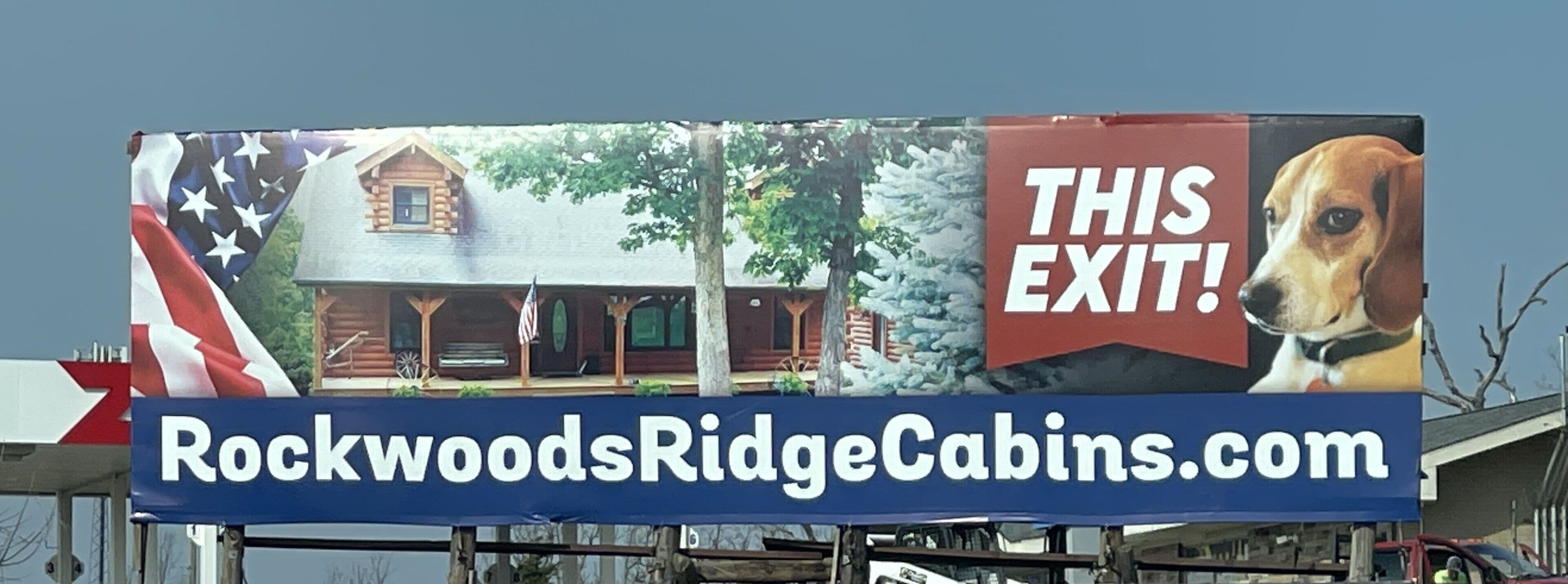 Un cartel publicitario de Rockwoods Ridge Cabins, con una imagen de una cabaña y una foto de un perro.